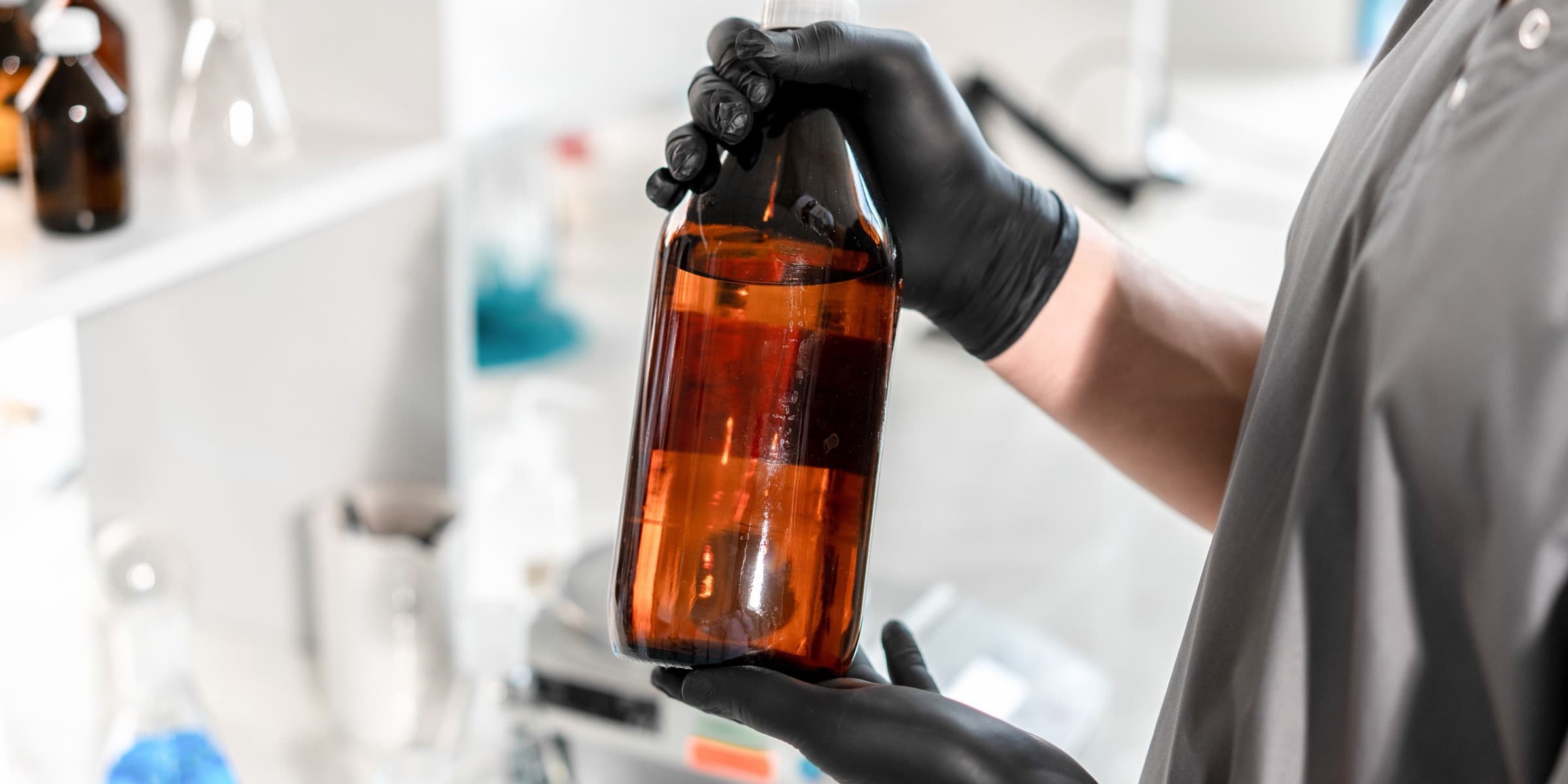Gloved hands holding a brown glass bottle